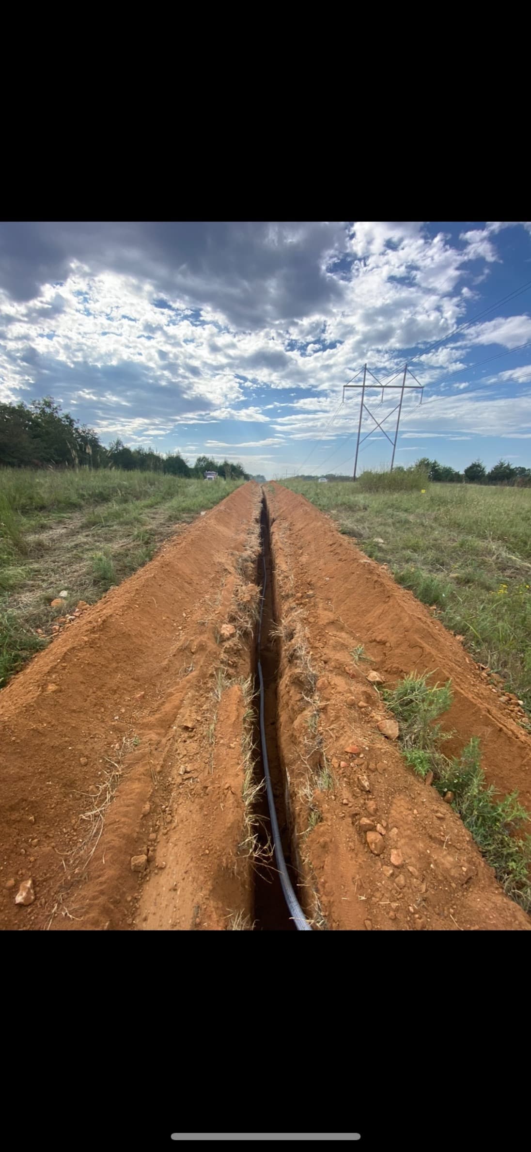 A narrow cable trench running to the horizon across open grassland beneath a transmission line